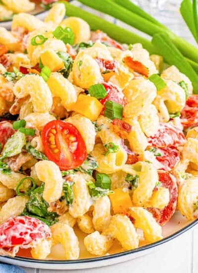Zoomed in on creamy bacon ranch pasta salad on a plate with green onions near the plate.
