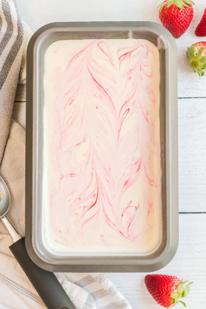 Loaf pan full of ice cream mixture from above swirled with strawberry swirls