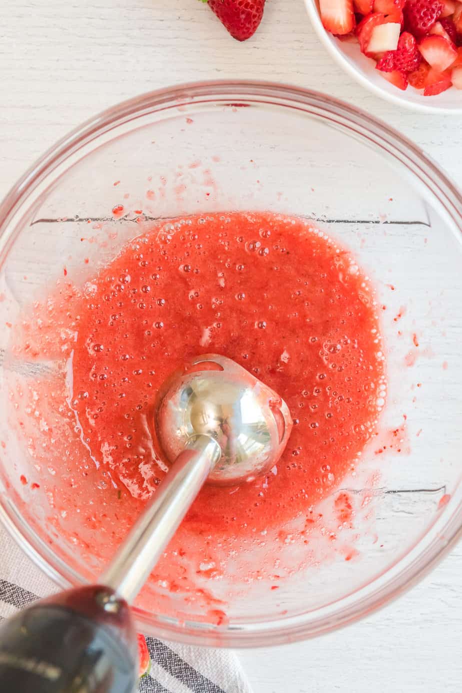Blending cooked strawberries in a large bowl with an immersion blender from above.