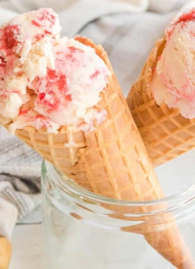 Strawberry swirl ice cream in two waffle cones resting in a glass jar from the side.