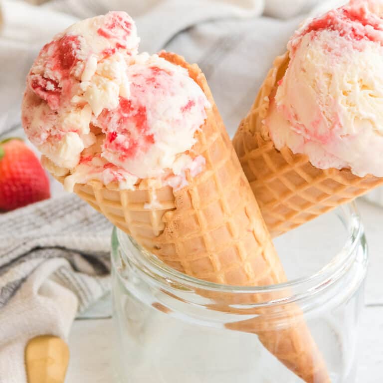 Strawberry swirl ice cream in two waffle cones resting in a glass jar from the side.