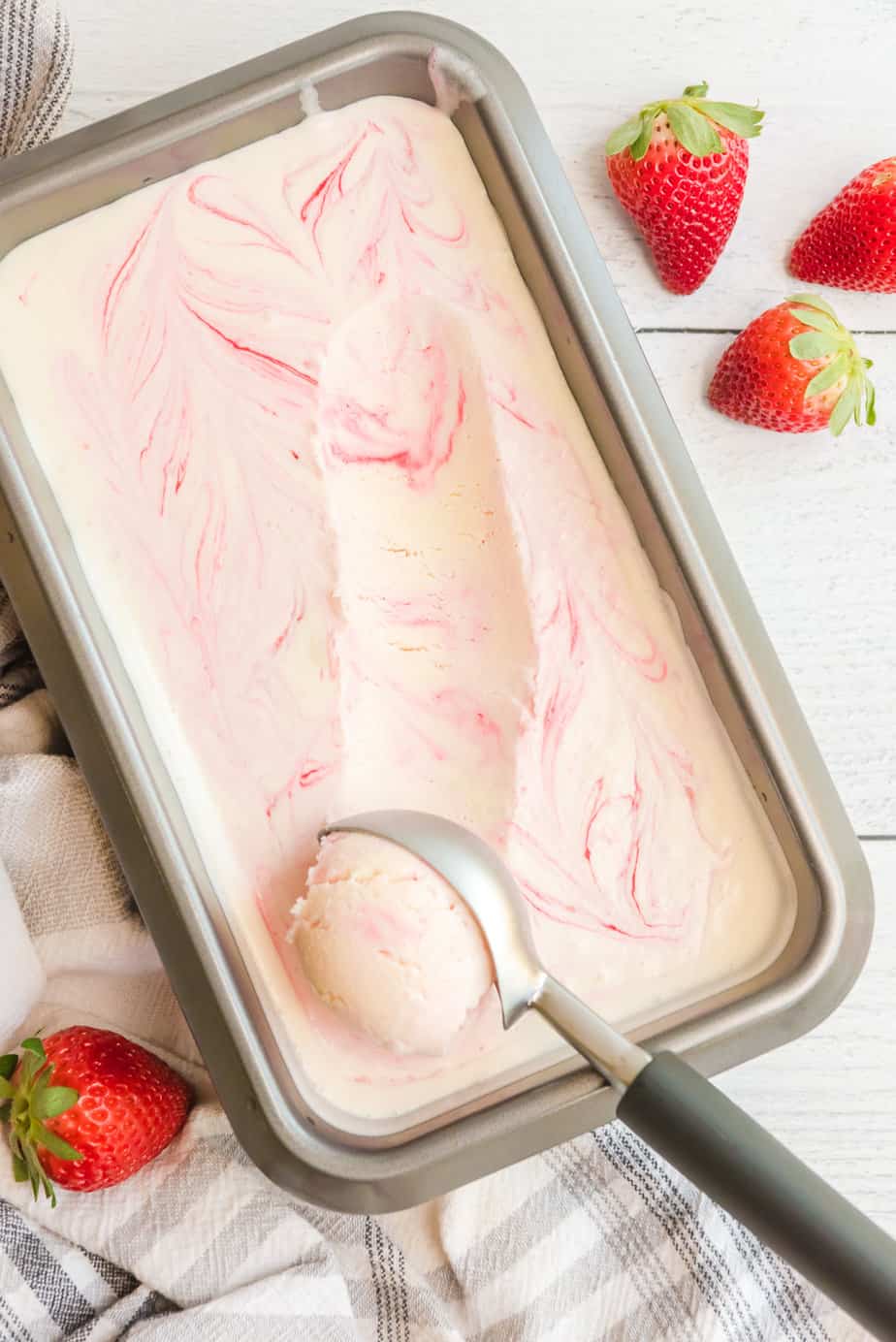 Vanilla ice cream with strawberry swirled through it being scooped out of a pan from overhead.