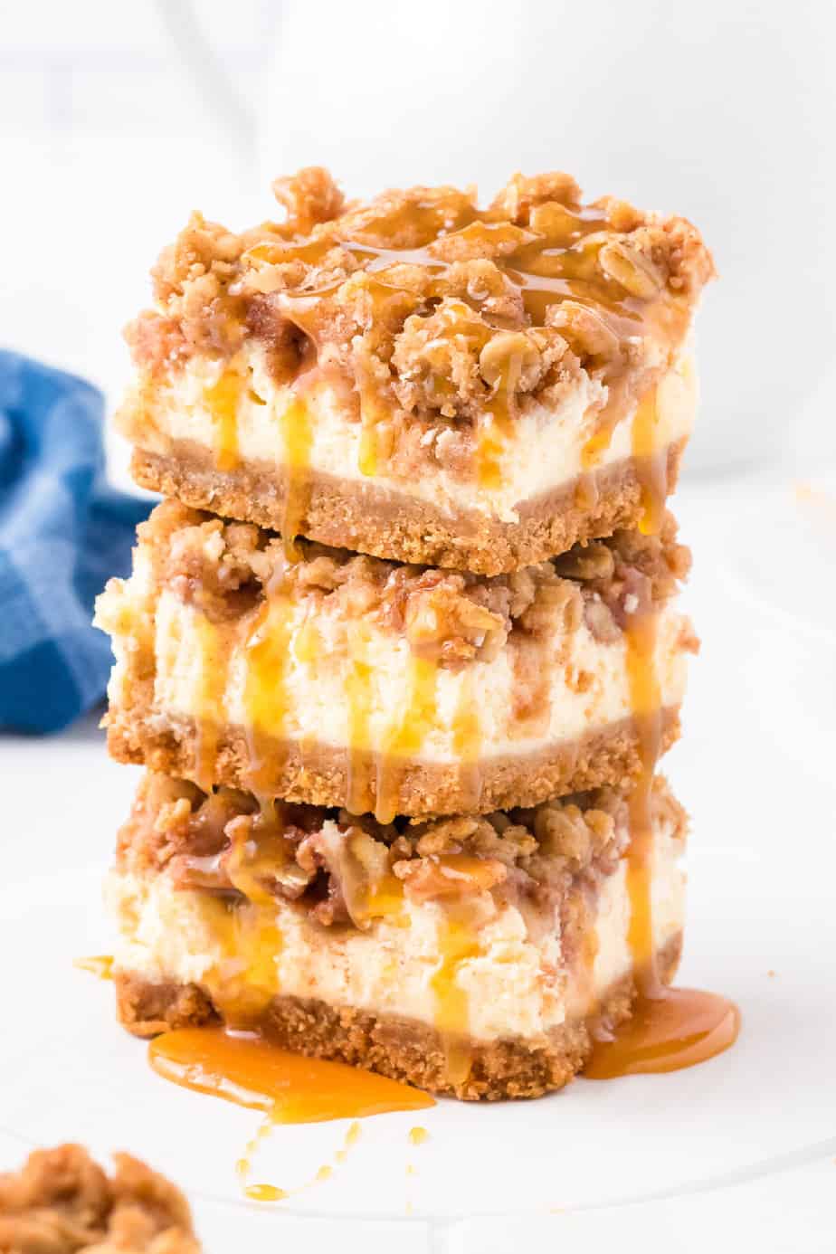 Tall stack of apple cheesecake bars from the side with caramel dripping down.