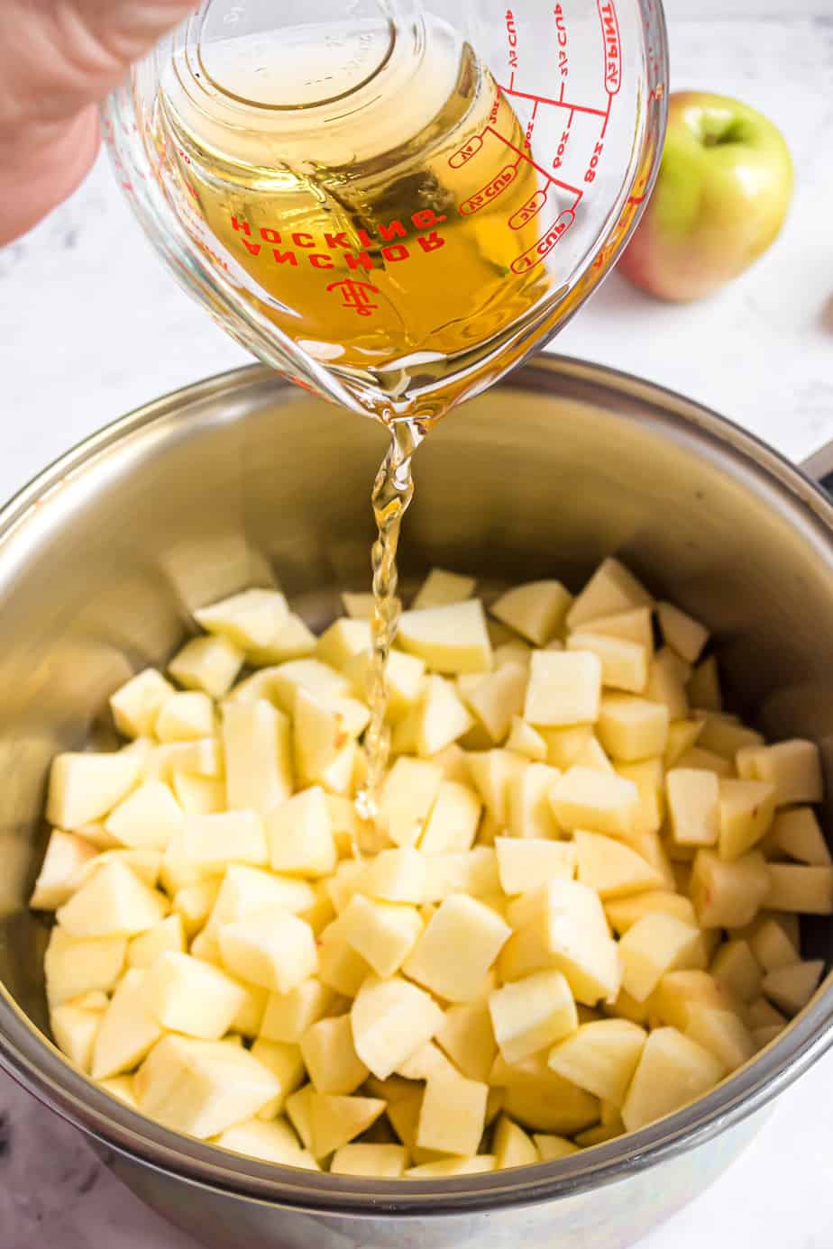 Apple juice being poured from a measuring cup into a pot full of diced apples.