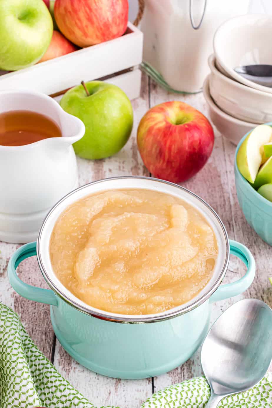 Applesauce in a small pot with fresh apples in the background on a table.