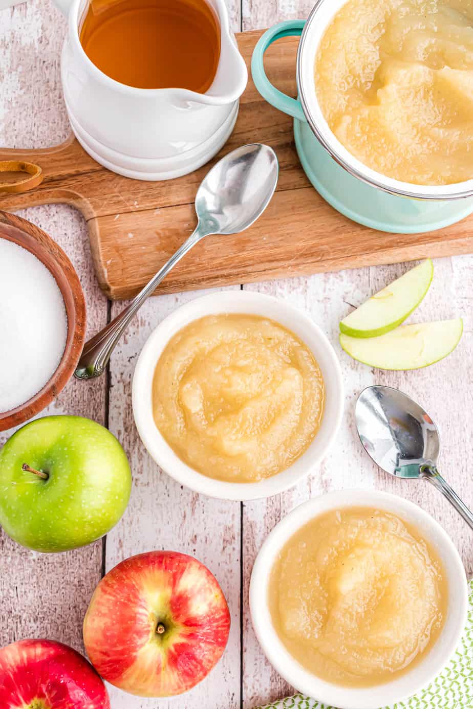 Applesauce portioned in bowls from overhead on a counter with fresh apples and spoons on the counter.