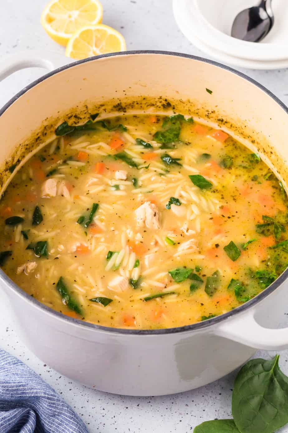 A large pot full of chicken lemon orzo soup with bits of spinach from a side angle looking into the pot.