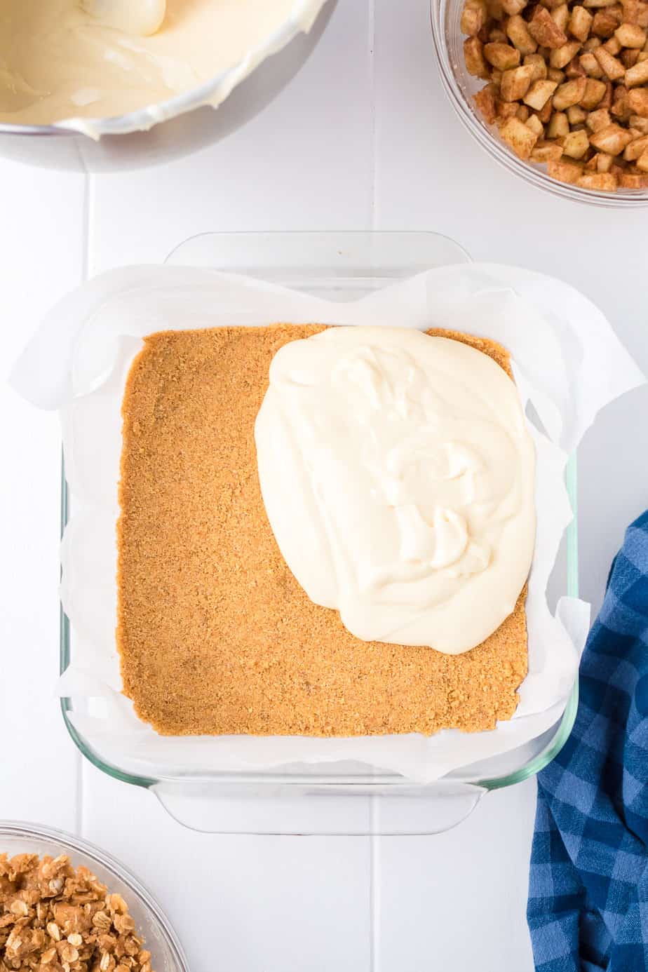 Spreading the cheesecake layer over the graham cracker crust in a square pan from overhead.