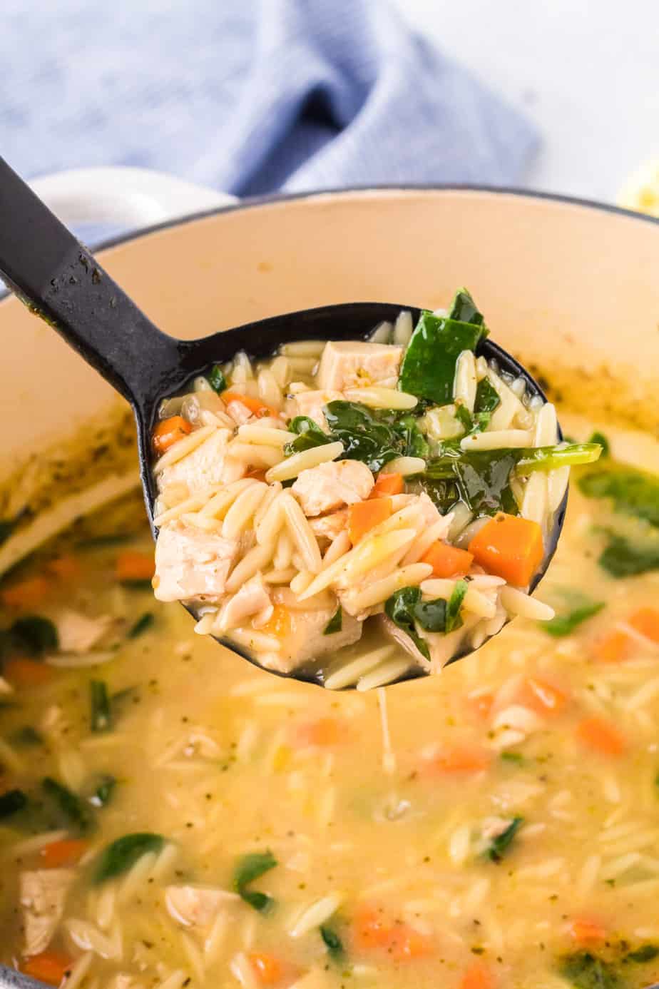 Ladle full of chicken lemon orzo soup pulling a scoop out of a pot.