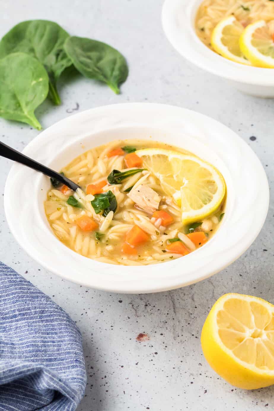 Chicken lemon orzo soup in a bowl from the side with a spoon and a slice of lemon in the bowl.