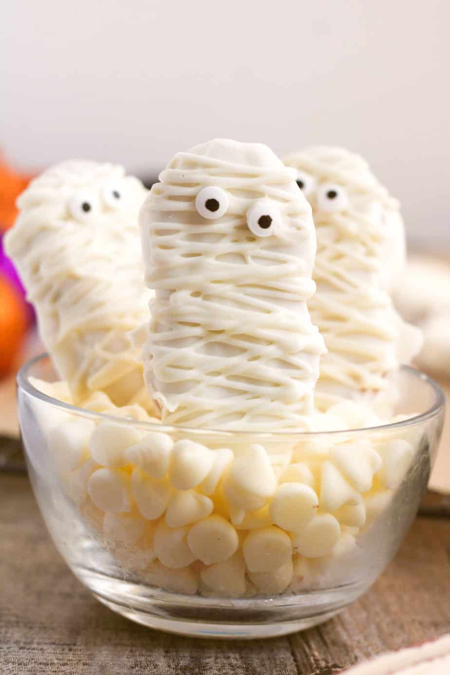 Three cookies decorated with white chocolate to look like mummies stacked upright in a serving bowl.