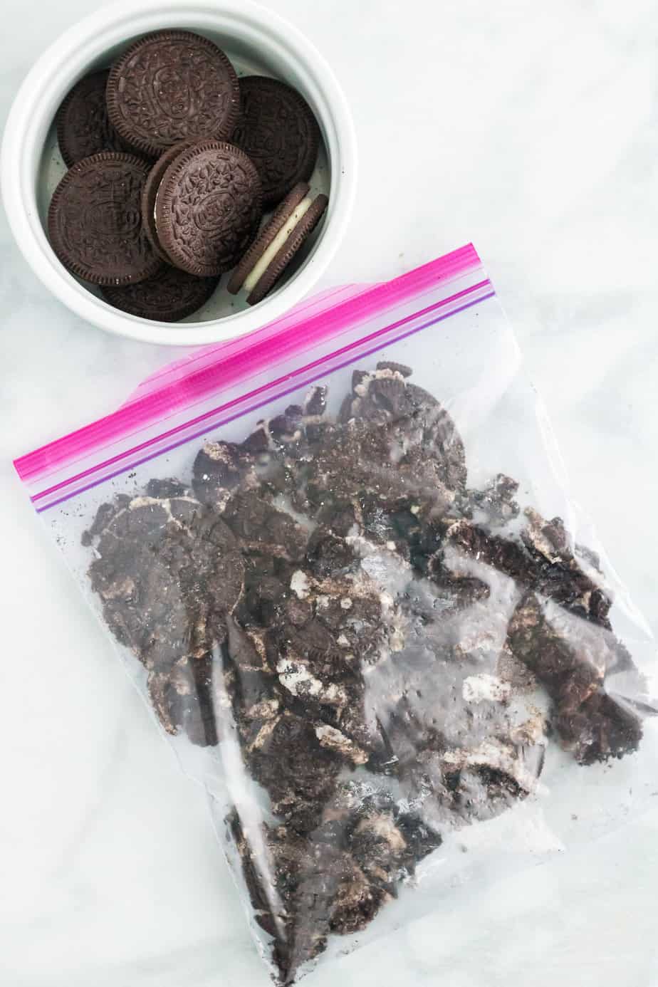 Crushing Oreo Cookies in a zip top bag with more Oreo cookies in a bowl nearby on the counter.