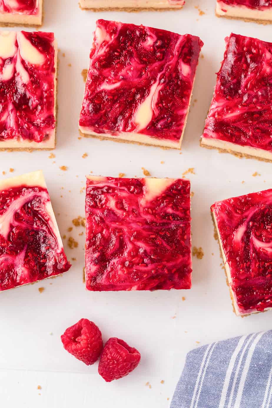 Raspberry cheesecake swirl bars placed from above on a table close up with fresh raspberries on parchment paper..