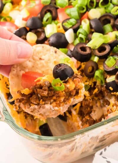 Chip dipping into layers of taco dip in a pan from the side.