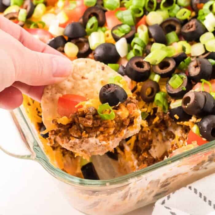 Chip dipping into layers of taco dip in a pan from the side.