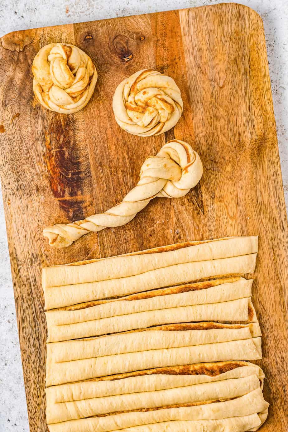 Twisting pumpkin crescent roll dough into knots from above on a cutting board.