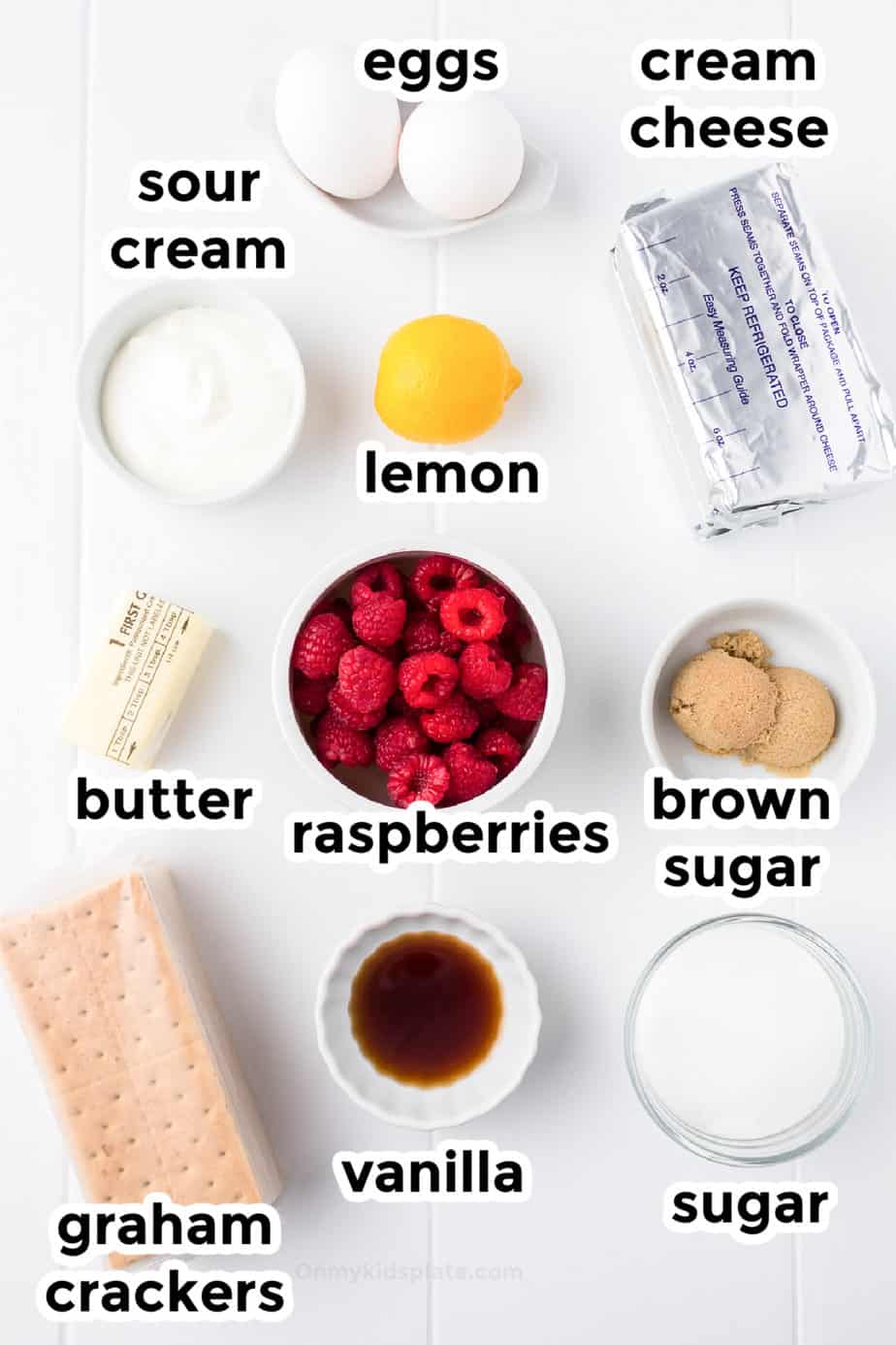 Ingredients for raspberry swirl cheesecake bars in bowls with labels on a counter from above.