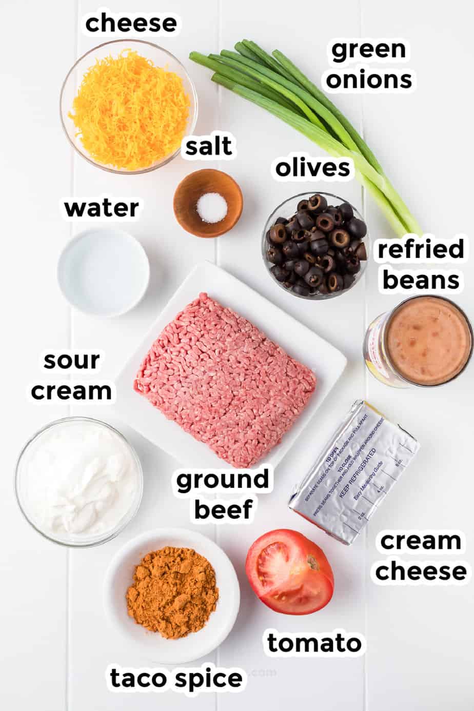 Ingredients for taco dip with ground beef in bowls from overhead on a counter with labels.