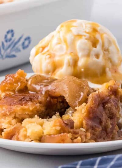 Caramel apple dump cake on a plate close up from the side topped with ice cream and more caramel on a plate.