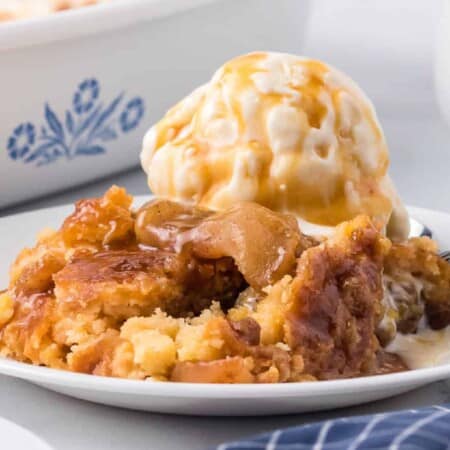 Caramel apple dump cake on a plate close up from the side topped with ice cream and more caramel on a plate.