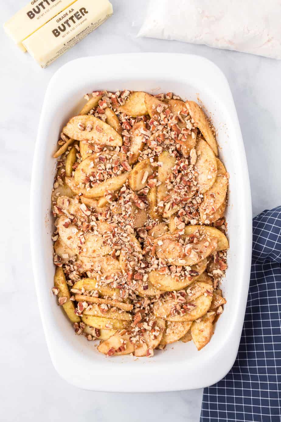 Apple slices mixed with cinnamon, sugar and pecans in a baking dish from overhead.