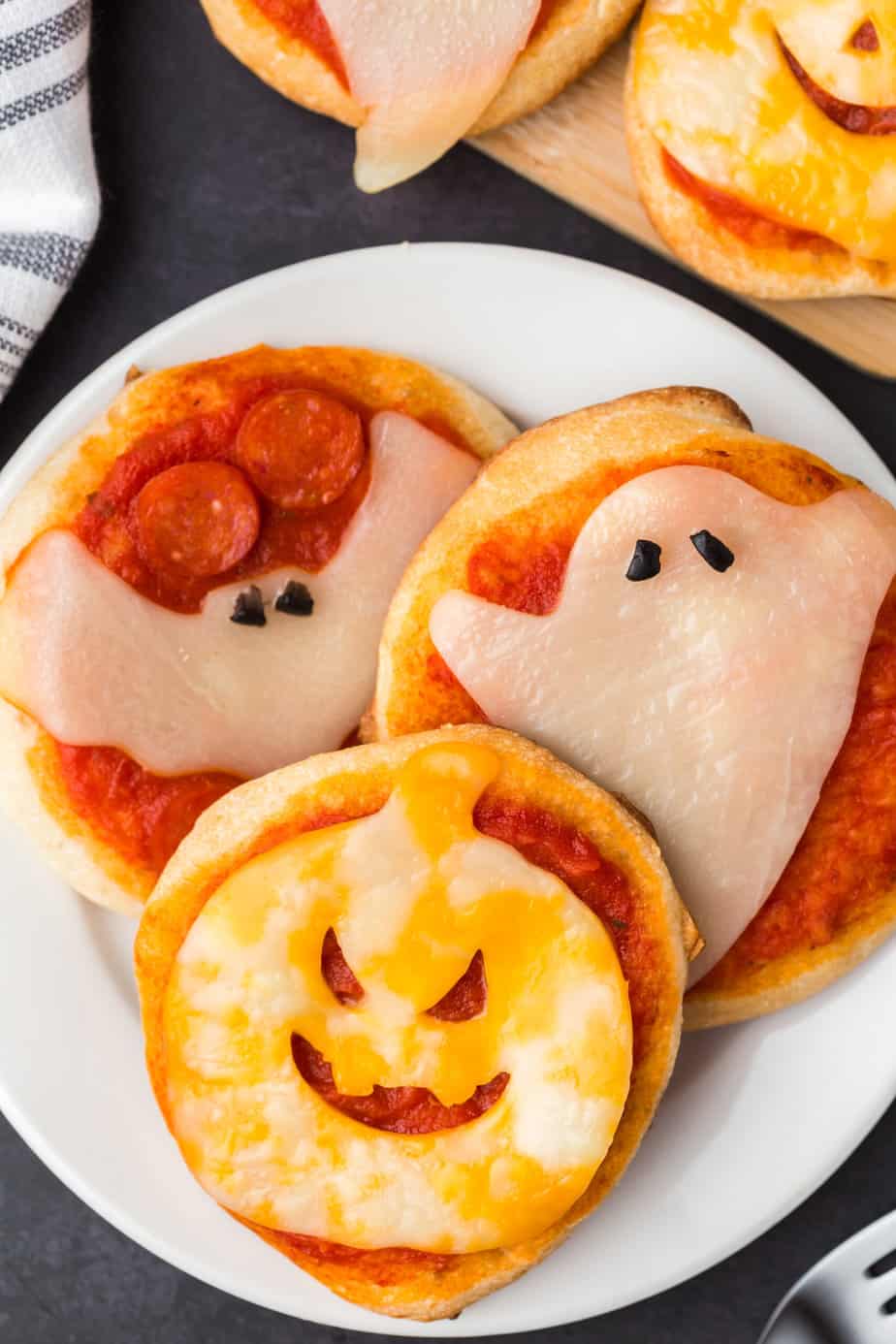Mini pizzas on a plate from overhead with cheese decorated like a bat, ghost and jack-o-lantern.