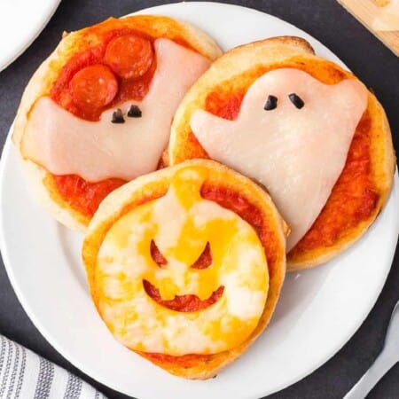 Mini pizzas on a plate decorated with cheese slices shaped to look like a bat, ghost and jack o lantern.