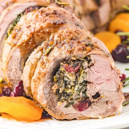 Close up of rolled pork tenderloin stuffed with spinach, cheese and dried fruit close up from the side with a few dried apricots and cranberries around the meat on the plate.