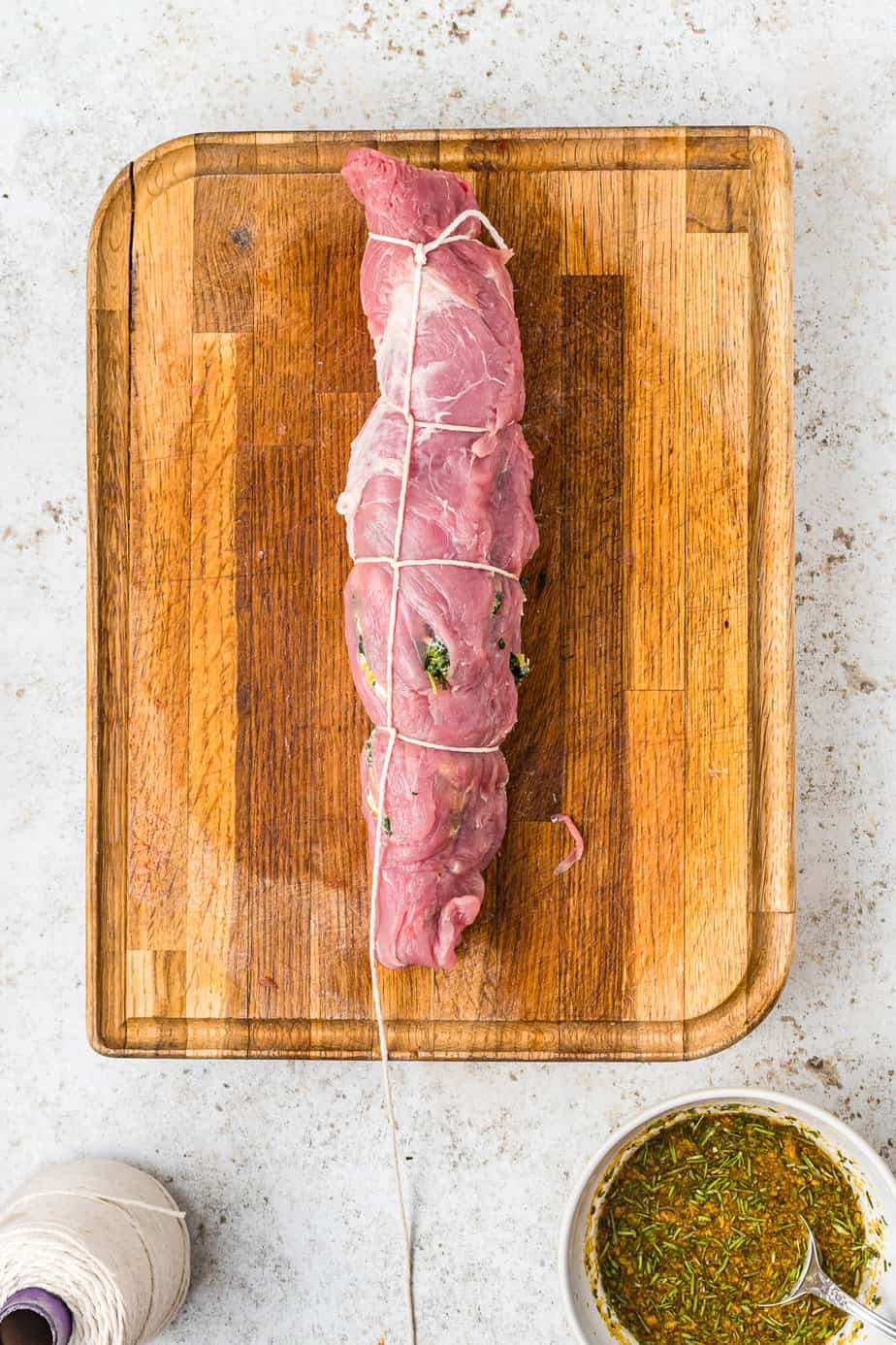 Pork tenderloin rolled and tied with butchers twine on a cutting board from overhead on a counter after being stuffed.