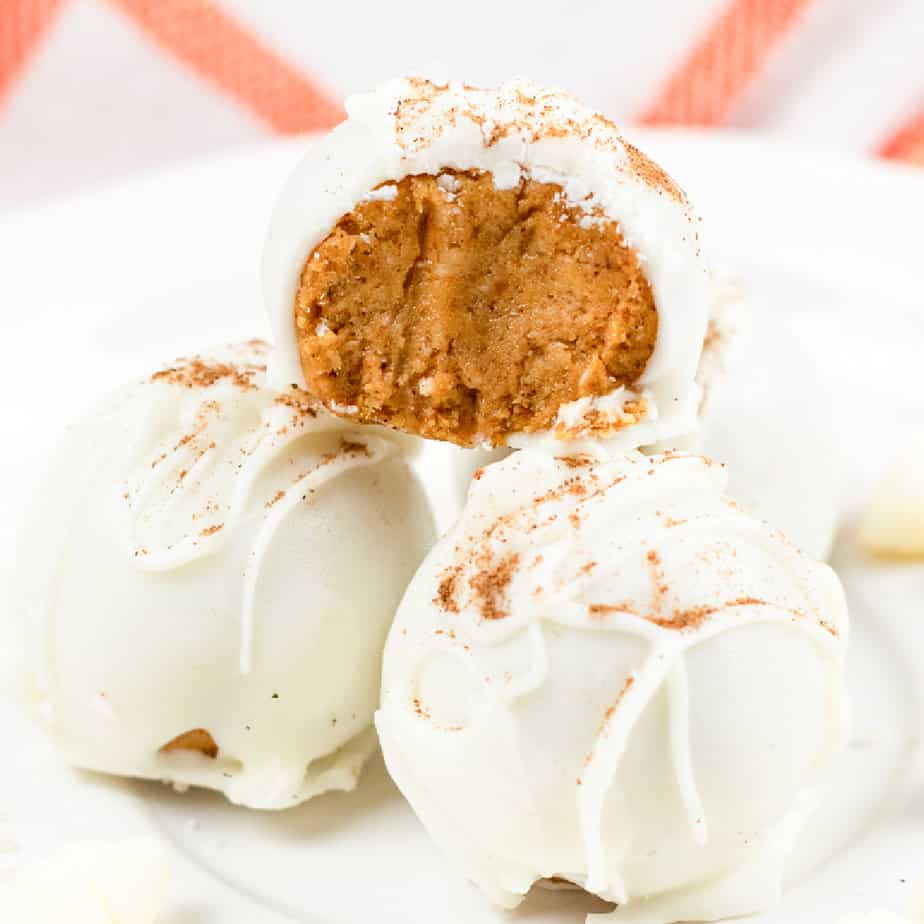 Up close side view of a pumpkin cheesecake bite stacked on top of two others coated in white chocolate with the top candy missing a bite on a white plate.