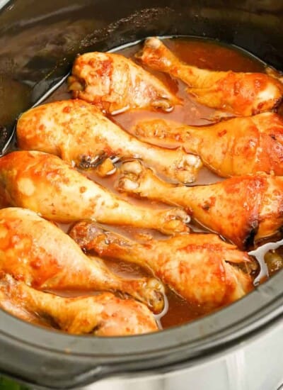Cooked chicken drumsticks in the slow cooker from the side in a brown sauce.