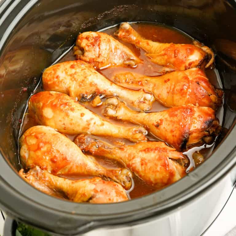 Cooked chicken drumsticks in the slow cooker from the side in a brown sauce.