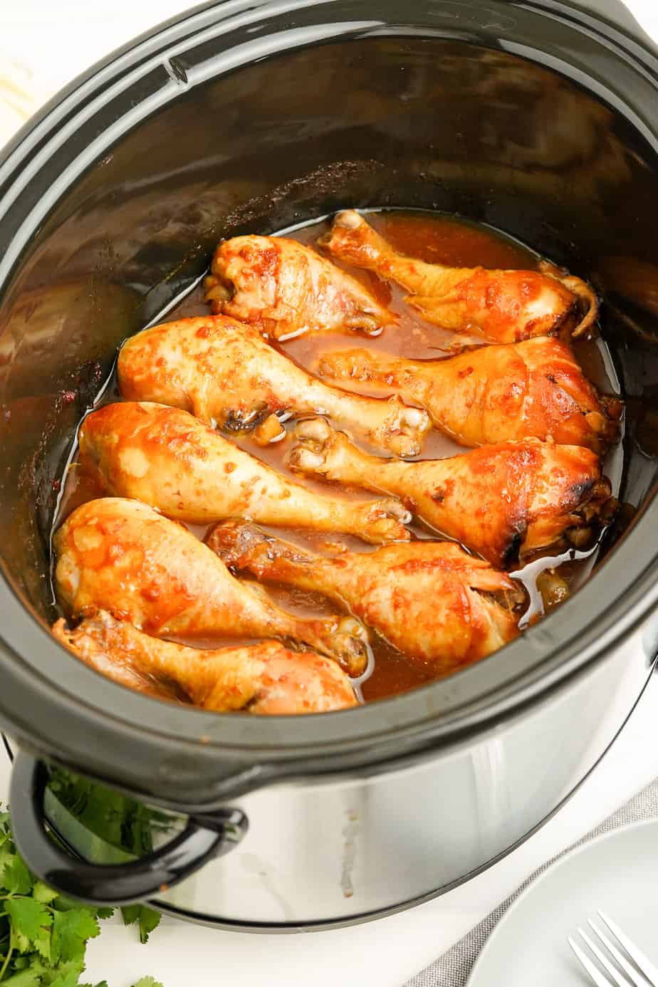 Chicken drumsticks cooked in a brown sauce in a slowcooker from the side.