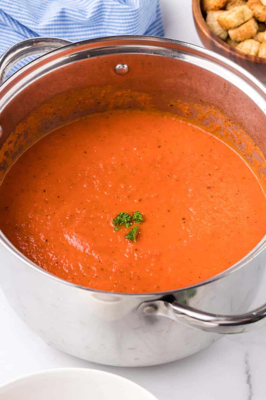 Creamy smooth tomato soup blended in a pot from the side.with a napkin and bowl edges nearby on the counter.