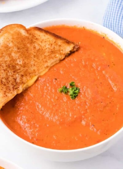 Side view of a bowl of tomato soup with a grilled cheese being dipped into the soup.