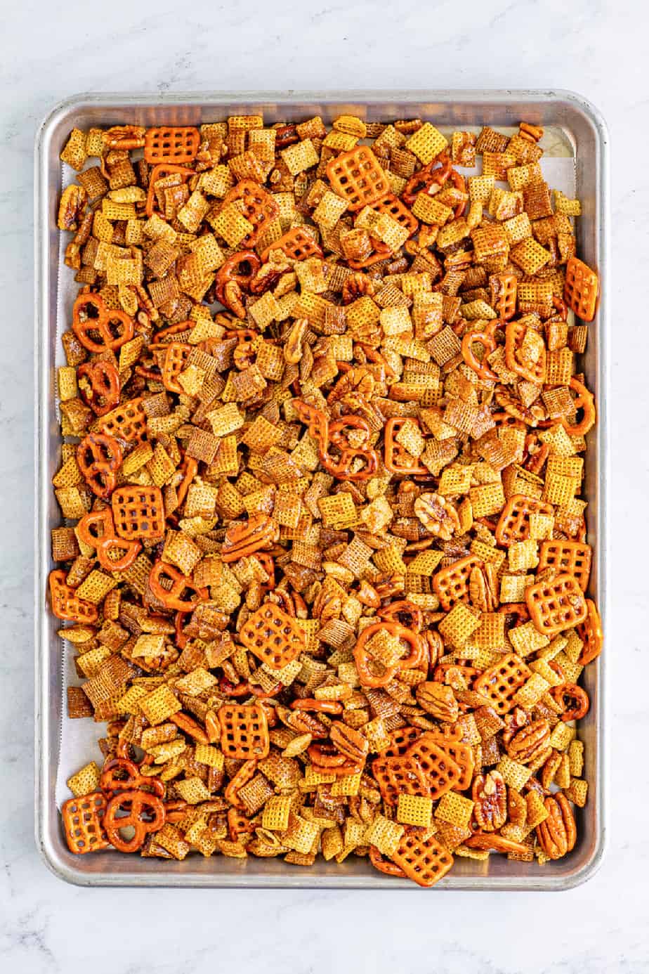 Chex cereal, pretzels, pecans after being baked on a sheetpan from overhead on the counter.