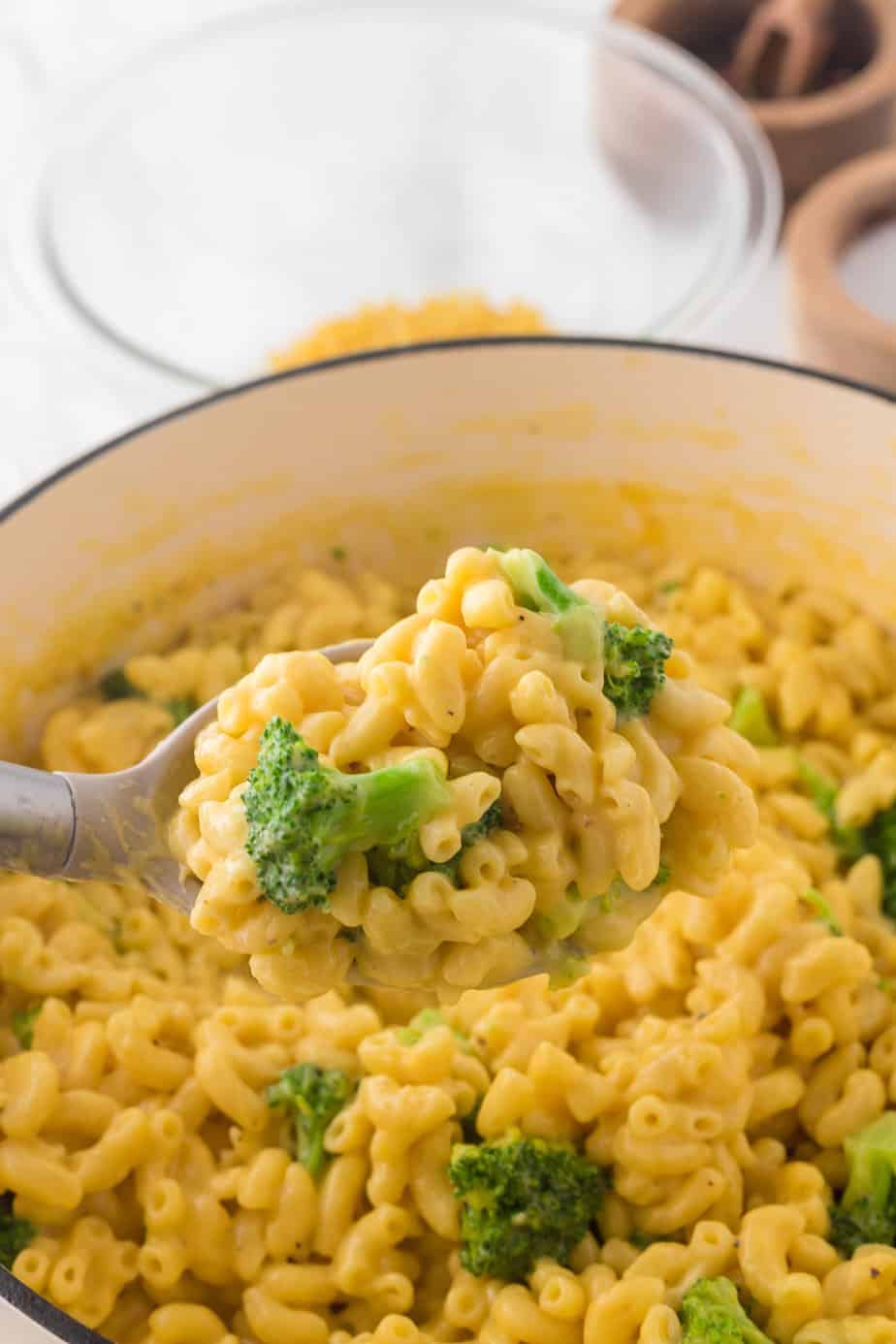 Close up on a full serving spoon full of mac and cheese with broccoli being scooped from a pot.