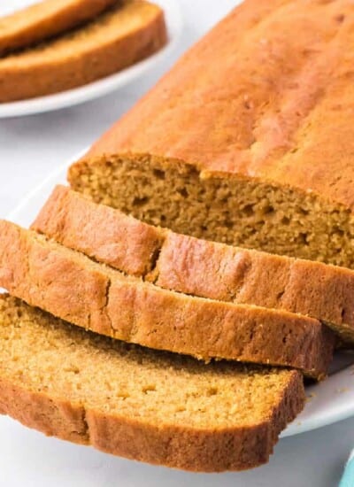 Sliced pumpkin loaf up close at an angle on a plate on a counter with a plate of two pumpkin bread slices behind.