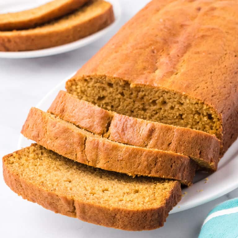 Sliced pumpkin loaf up close at an angle on a plate on a counter with a plate of two pumpkin bread slices behind.