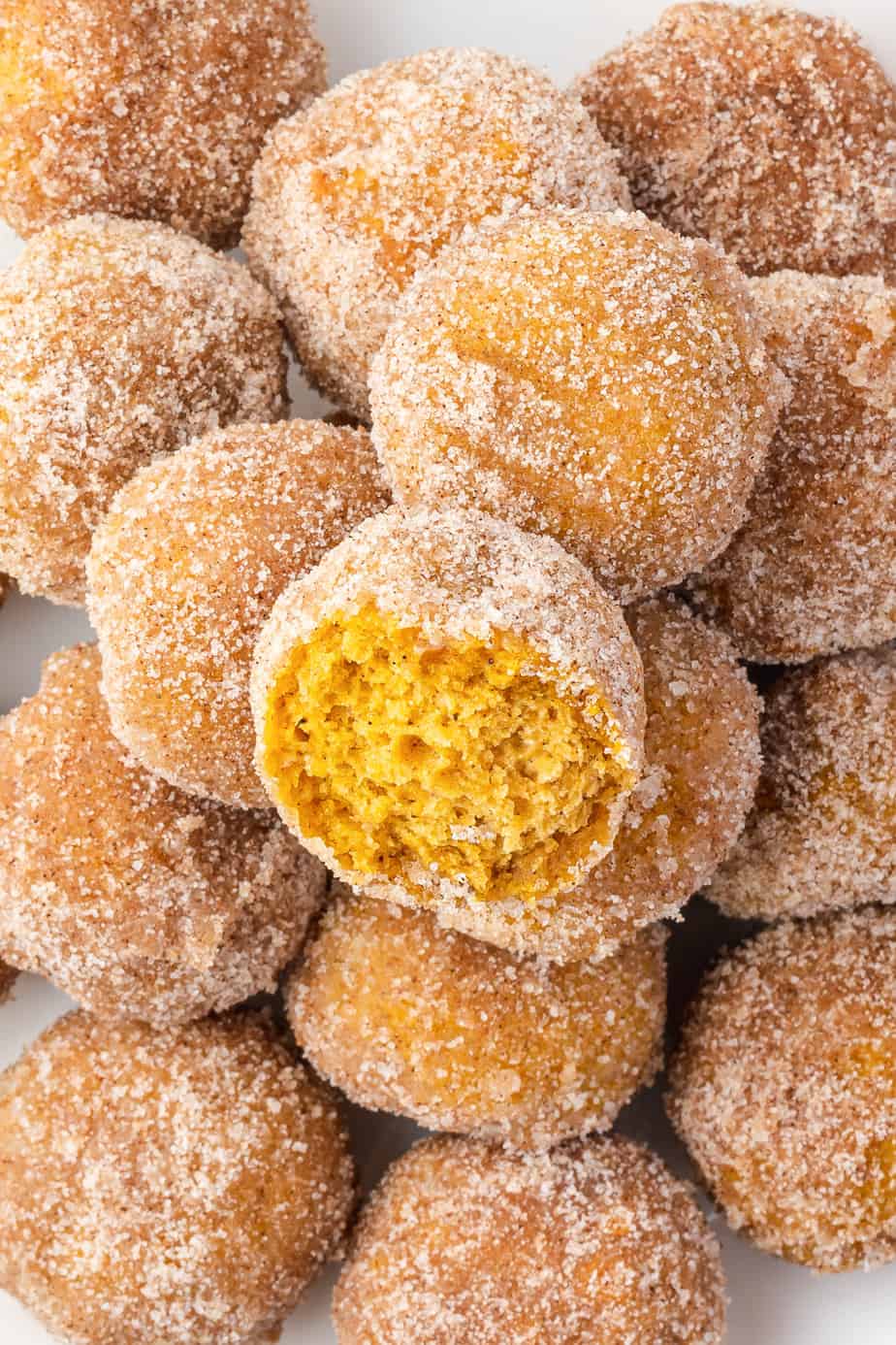 Close up of a stack of pumpkin donut holes with the top one missing a bite.