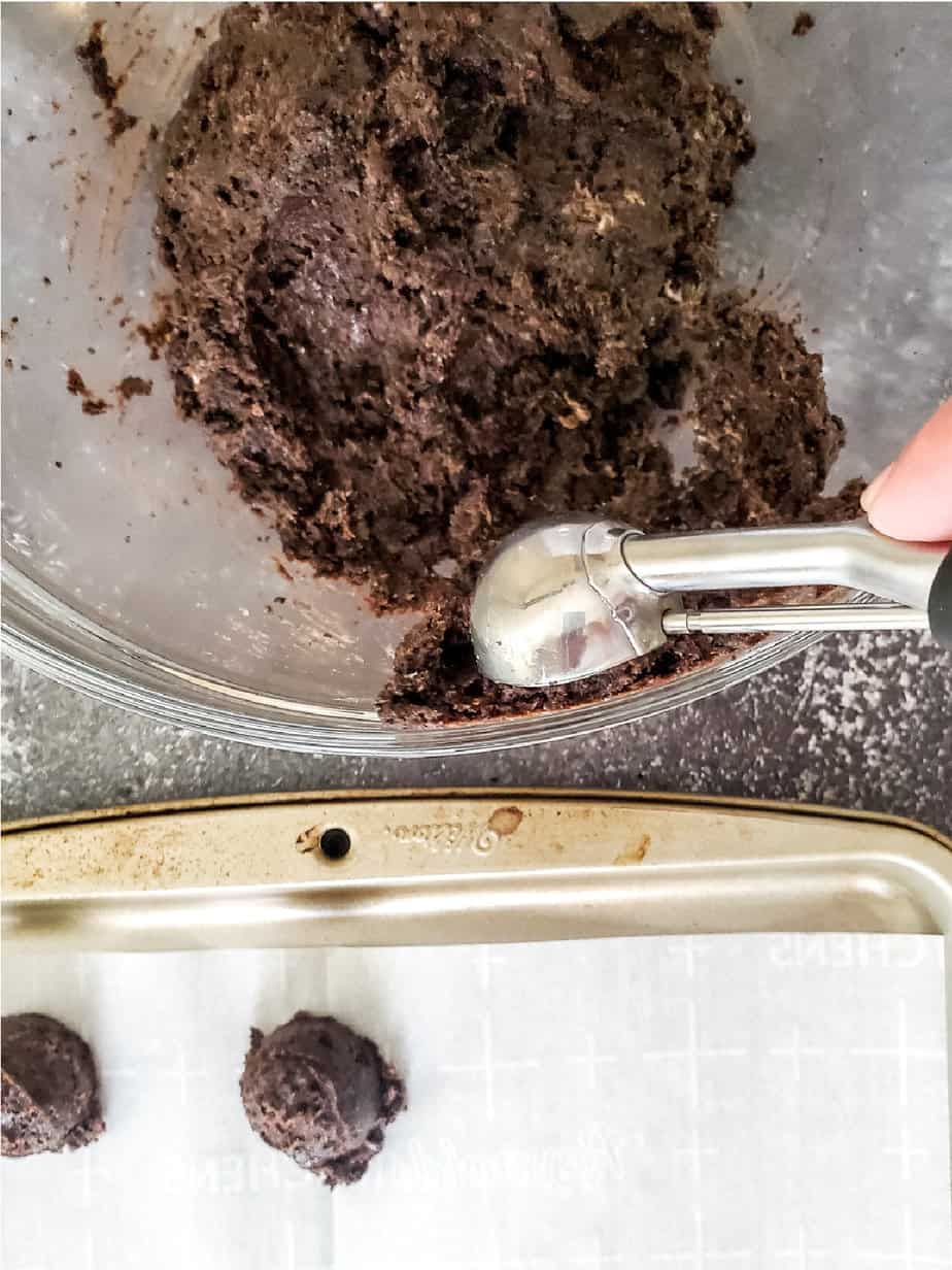 Scooping chocolate truffle mix from a bowl from overhead and rolling into balls put on a parchment paper lined pan.