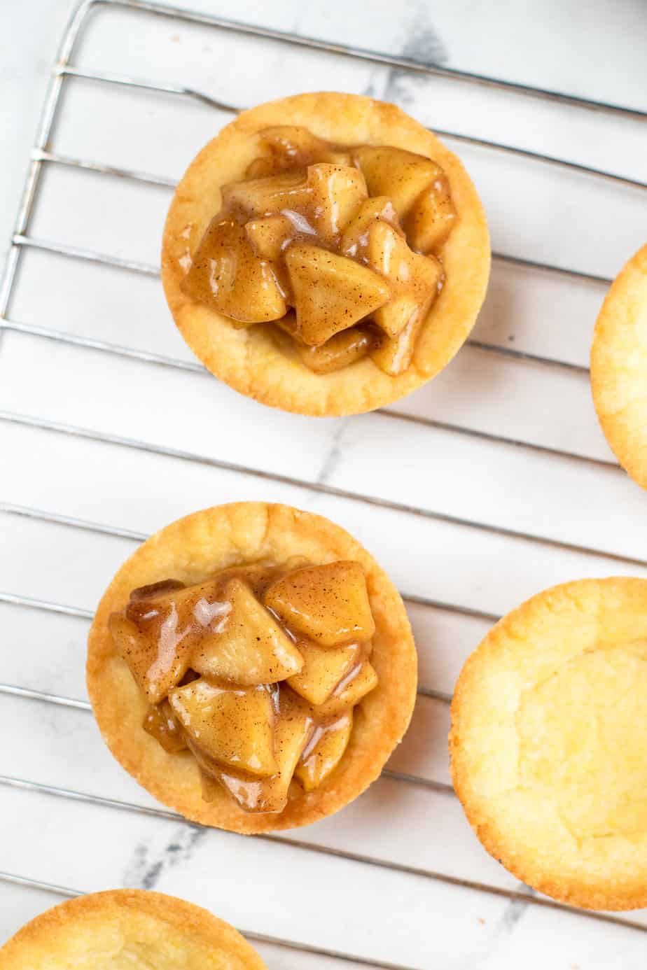 Sugar cookie cups full of apple filling up close from overhead on a wire rack on a counter.