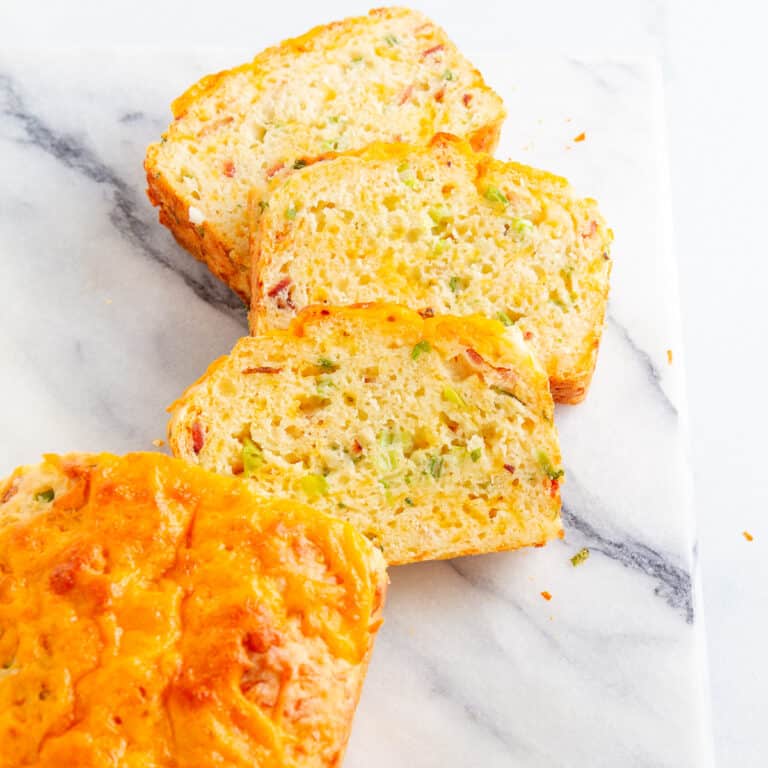 Three slices bacon cheddar bread from overhead next to part of the loaf on a marble cutting board.