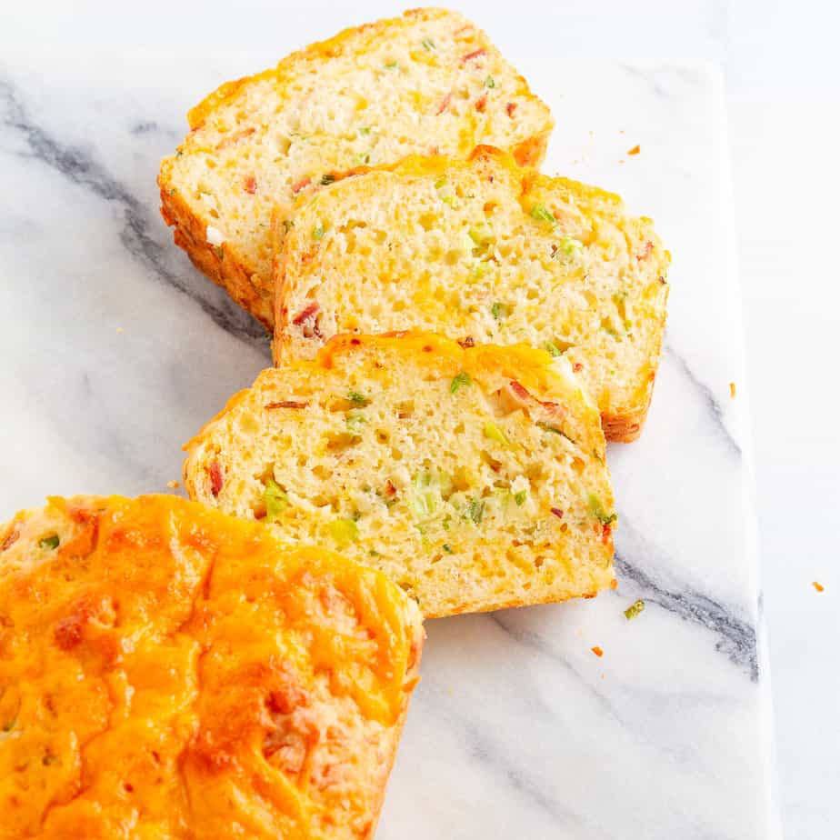 Three slices bacon cheddar bread from overhead next to part of the loaf on a marble cutting board.