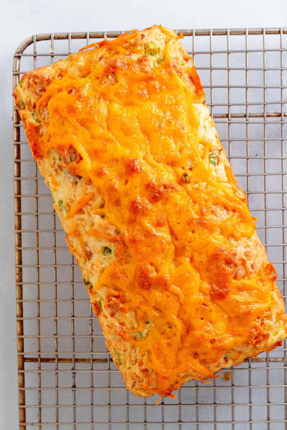 Loaf bread from above with cheese melted over the top resting on a wire rack on the counter.