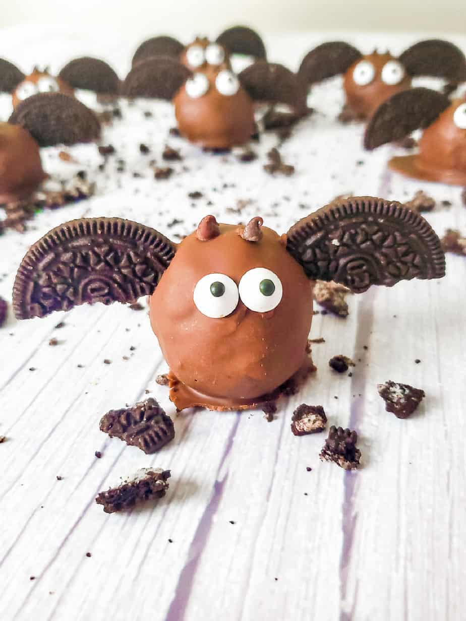 Chocolate Oreo ball decorated like a bat with cookie wings from the side with more in the background.