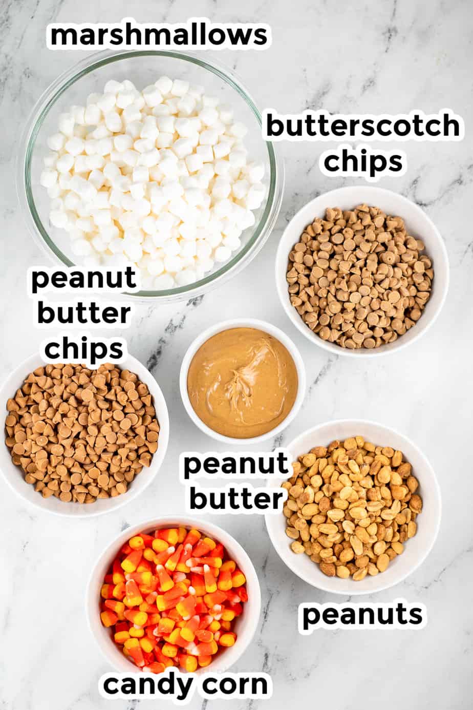 Ingredients for candy corn peanut butter bars in bowls on a counter from overhead on a counter with text title labels,