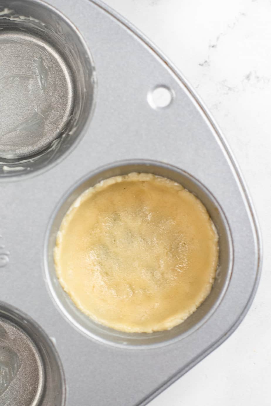 Up close of a muffin pan from overhead with cookie dough pressed into a cup formation with the muffin pan from overhead on a kitchen counter.