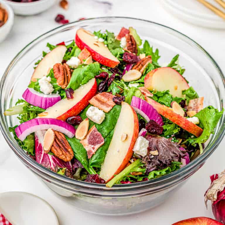 Large glass bowl full of apple cranberry salad mixed with purple onion, feta cheese and pecans.