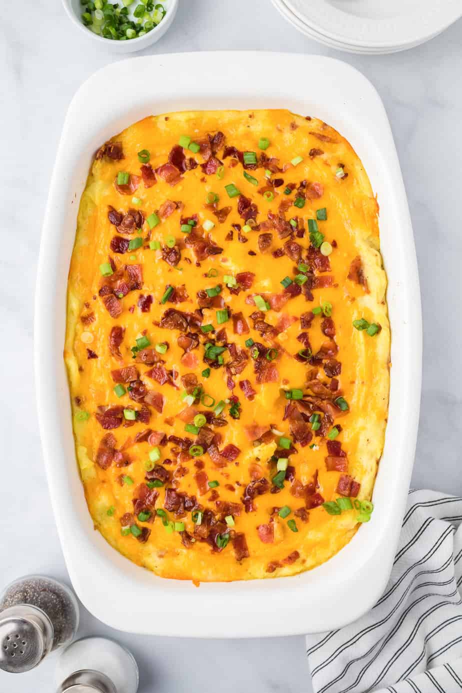 Baked loaded mashed potato casserole from overhead in a pan on a counter covered in cheese, bacon and green onions.